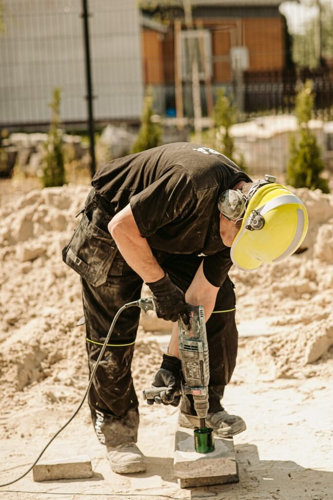 Construction worker using a demolition hammer outdoors during a sunny day.
