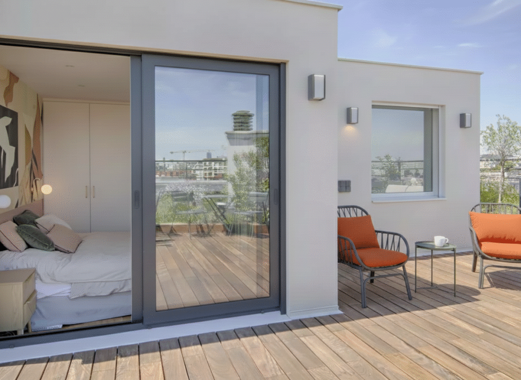 Surélévation de maison contemporaine avec terrasse bois et baie vitrée menant à une chambre